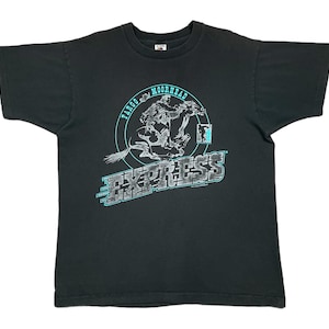 Puede incluir: Camiseta gris oscuro con un gráfico. El gráfico presenta un vaquero montando a caballo, con el texto "FARGO MOORHEAD EXPRESS" en verde azulado y gris. La camiseta es de estilo cuello redondo clásico.