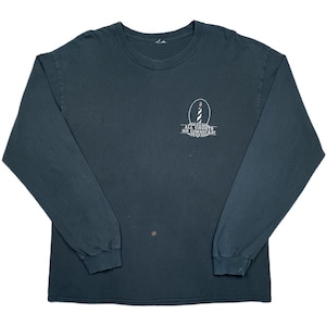 May include: Dark teal long-sleeve shirt with a crew neck. The shirt features a small graphic of a lighthouse with the text "ALL GHOSTS NO GIMMICKS!" in white. The shirt is made of a soft, comfortable material.
