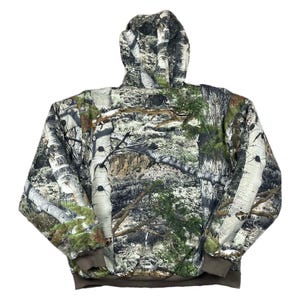 May include: A hooded jacket with a camouflage pattern featuring birch tree bark, green foliage, and brown accents. The jacket has a brown ribbed hem and cuffs. The hood is fully lined with the same camouflage pattern.