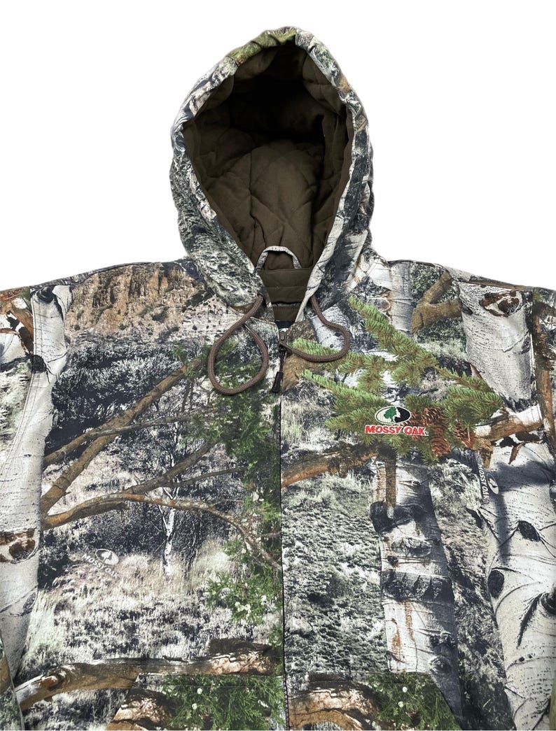 May include: A hooded camouflage jacket with a drawstring closure. The jacket features a forest pattern with shades of green, brown, and white. The Mossy Oak logo is visible on the front. The interior lining is a solid brown color.