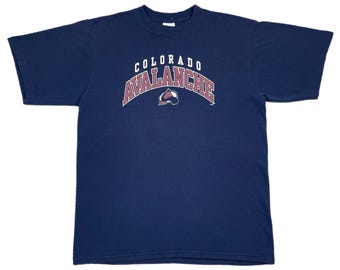 May include: Navy blue t-shirt featuring the text "COLORADO AVALANCHE" in a curved, maroon and white design. The shirt also displays the team's logo. The t-shirt is made of a soft material.