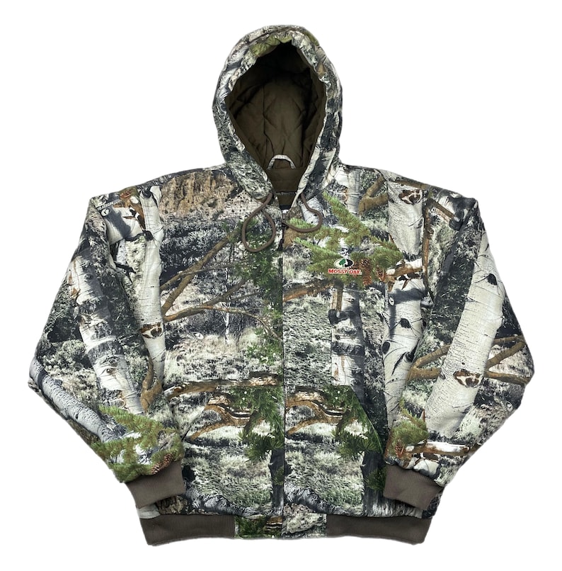 May include: A hooded camouflage jacket with a forest pattern. The jacket features a full-length zipper, a drawstring hood, and a brown ribbed hem and cuffs. The Mossy Oak logo is visible on the chest.