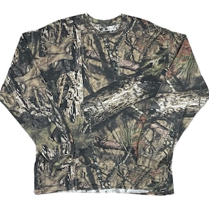May include: Long-sleeved camouflage shirt in shades of brown, green, and gray. The shirt features a crew neck and a pattern designed to blend with a wooded environment. The fabric appears to be a medium-weight material.