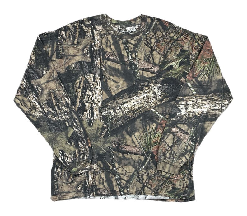 May include: Long-sleeved camouflage shirt in shades of brown, green, and gray. The shirt features a crew neck and a pattern designed to blend with a wooded environment. The fabric appears to be a medium-weight material.