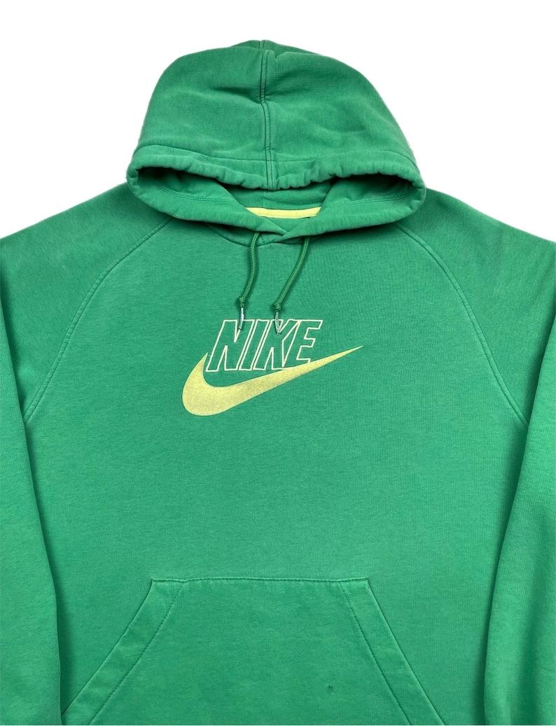 May include: Green Nike hoodie with a yellow Nike logo on the front. The hoodie has a hood with a drawstring and a front pocket. The Nike logo is a swoosh and the word "NIKE" in a sans-serif font.