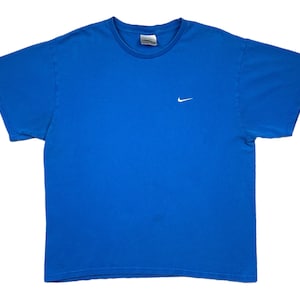 Puede incluir: Una camiseta azul liso con cuello redondo y mangas cortas. Un peque&ntilde;o logotipo blanco de Nike est&aacute; bordado en el pecho izquierdo. La camiseta est&aacute; hecha de un material suave, probablemente algod&oacute;n.