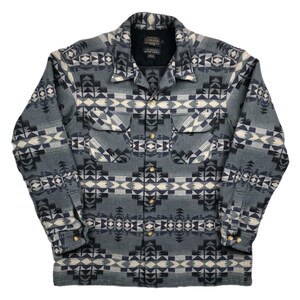 Pode incluir: Uma camisa Pendleton de manga comprida azul e branca com um padrão geométrico. A camisa tem um fecho de botões na frente e dois bolsos no peito.