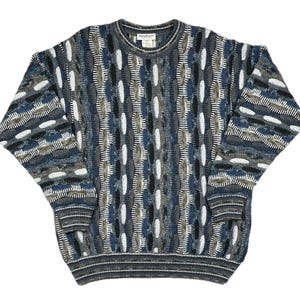 May include: A multi-colored sweater with a unique textured pattern. The sweater features a mix of blue, gray, white, and brown hues. It has a crew neck and long sleeves, with ribbed cuffs and hem. The overall design is a blend of geometric and organic shapes.