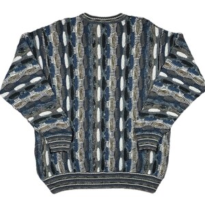 May include: A patterned sweater in shades of blue, grey, white, and brown. The design includes oval shapes and vertical lines. The long-sleeved sweater has a ribbed hem and cuffs. The sweater is a classic style.