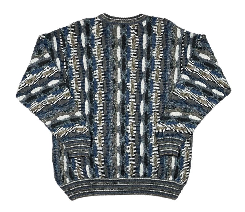 May include: A patterned sweater in shades of blue, grey, white, and brown. The design includes oval shapes and vertical lines. The long-sleeved sweater has a ribbed hem and cuffs. The sweater is a classic style.