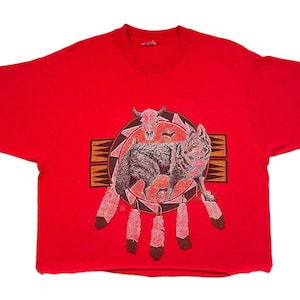 Peut inclure: T-shirt rouge avec une illustration de loup et un motif amérindien. Le motif comprend un loup, un crâne, des plumes et des motifs géométriques bruns, rouges et noirs.