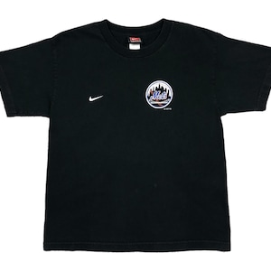 Puede incluir: Camiseta negra con el logo de los Mets de Nueva York en la parte delantera. El logo es un diseño circular con el nombre del equipo y un paisaje urbano. Un logotipo de Nike es visible en el pecho izquierdo.