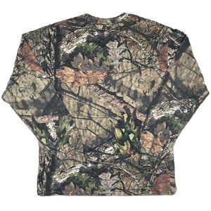 May include: Long-sleeved camouflage shirt in shades of brown, green, and tan. The shirt features a crew neck and a pattern designed to blend with natural environments. The fabric appears to be a lightweight material, suitable for outdoor activities.