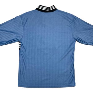 May include: A light blue short-sleeved jersey with a ribbed texture. The collar is black with white stripes, and there are black and white stripes on the sleeves. The jersey is viewed from the back.