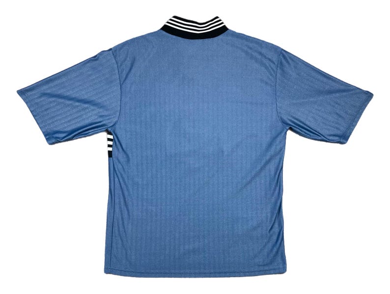 May include: A light blue short-sleeved jersey with a ribbed texture. The collar is black with white stripes, and there are black and white stripes on the sleeves. The jersey is viewed from the back.