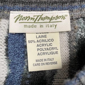 May include: Close-up of a sweater tag from Norrm Thompson, made in Italy. The tag lists the materials as wool and acrylic. The sweater has a blue, grey, and white striped pattern.