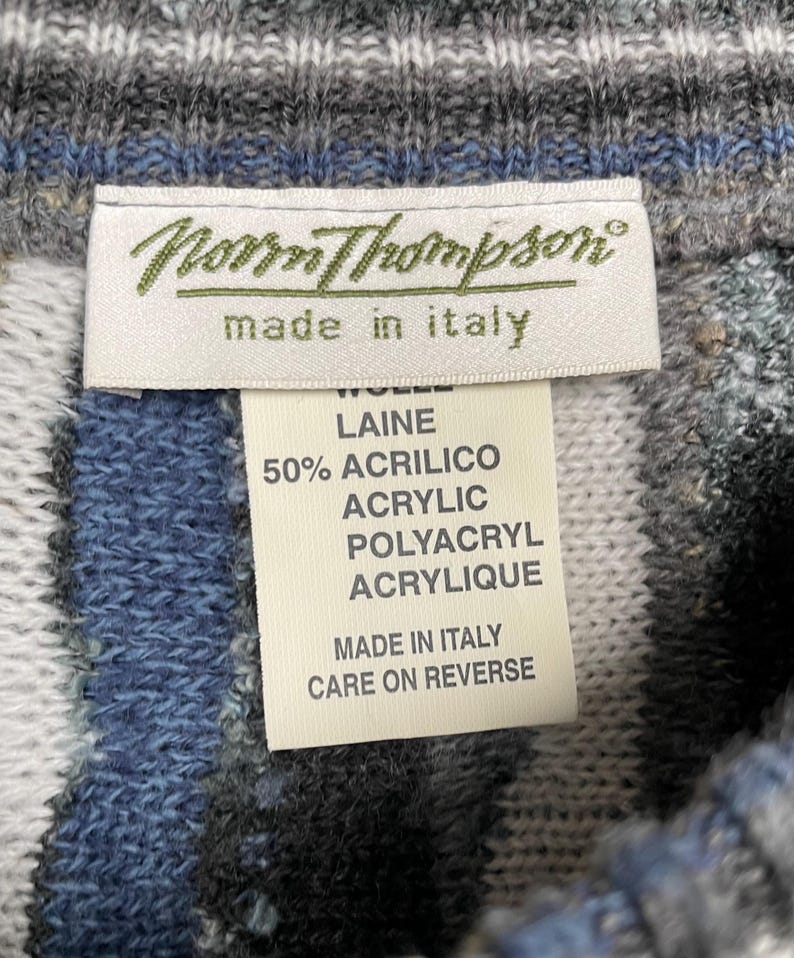 May include: Close-up of a sweater tag from Norrm Thompson, made in Italy. The tag lists the materials as wool and acrylic. The sweater has a blue, grey, and white striped pattern.