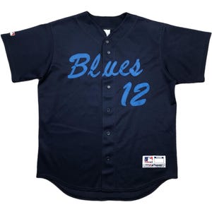 May include: Navy blue baseball jersey with the word "Blues" in light blue script across the chest, along with the number "12". The jersey has a button-up front and a small tag at the bottom. The jersey is made of a mesh material.