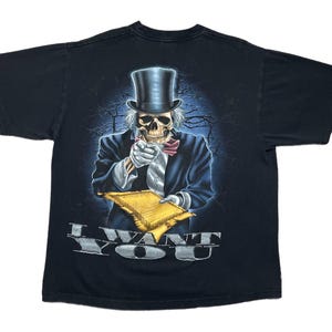 Könnte beinhalten: Schwarzes T-Shirt mit einer skelettartigen Figur in Zylinder und Anzug, die auf den Betrachter zeigt. Die Figur hält eine Schriftrolle, darunter steht "I WANT YOU". Das Design hat einen dunklen, detaillierten Illustrationsstil.