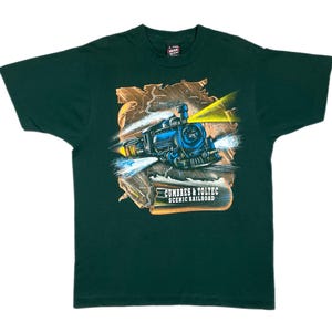 May include: Dark green t-shirt with a detailed illustration of a blue steam train with yellow and white light effects. The train is set against a brown and tan landscape with the text "Cumbres & Toltec Scenic Railroad".