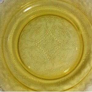 Pu&ograve; includere: Un piatto di vetro giallo con un motivo decorativo di fiori e foglie. Il piatto ha un bordo ondulato e un centro rialzato.