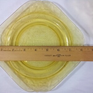 Pu&ograve; includere: Un piatto di vetro giallo con un bordo smerlato e un motivo floreale. Il piatto ha un diametro di 15 cm.