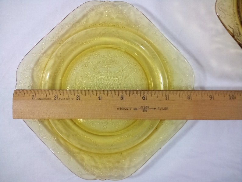 Pu&ograve; includere: Un piatto di vetro giallo con un bordo smerlato e un motivo floreale. Il piatto ha un diametro di 15 cm.