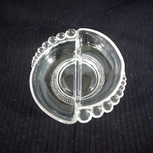 Può includere: Un piatto da portata in vetro trasparente diviso con un bordo perlato. Il piatto è diviso in due sezioni.