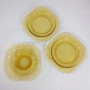 Pu&ograve; includere: Tre ciotole di vetro ambrato di forma quadrata con un bordo rialzato. Le ciotole presentano un delicato design inciso e sono perfette per servire dessert o spuntini.