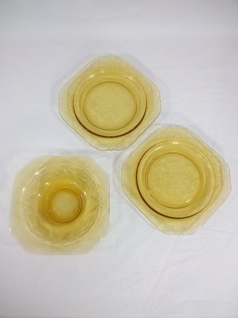 Pu&ograve; includere: Tre ciotole di vetro ambrato di forma quadrata con un bordo rialzato. Le ciotole presentano un delicato design inciso e sono perfette per servire dessert o spuntini.