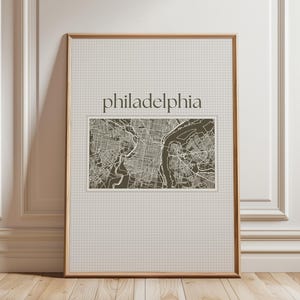 Può includere: Una stampa incorniciata di una mappa di Philadelphia, Pennsylvania. La mappa è in bianco e nero e mostra le strade e i monumenti della città. La parola "philadelphia" è stampata in nero nella parte superiore della stampa.