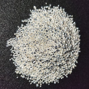 Peut inclure: Gros plan sur un tas de petites perles brillantes de couleur argentée. Les perles sont regroupées sur une surface sombre et texturée, créant un aspect réfléchissant et texturé. Les perles varient en taille, ajoutant un intérêt visuel.
