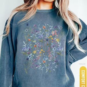 May include: Blue jean colored sweatshirt with a floral design. The sweatshirt features a cluster of colorful flowers in shades of purple, yellow, and pink. The text "COMFORT COLORS" and "BLUE JEAN" are visible on the image.