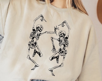 May include: A cream colored sweatshirt with a black graphic of two skeletons dancing. The sweatshirt has a relaxed fit and long sleeves.