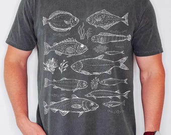 May include: A charcoal gray short-sleeve t-shirt featuring a white line-art graphic print of various fish species and aquatic plants arranged across the front. The shirt has a crew neckline and a faded, washed-out fabric texture.