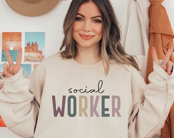 May include: A beige sweatshirt with the text "social worker" printed in colorful letters. The letters are in shades of purple, green, and yellow.