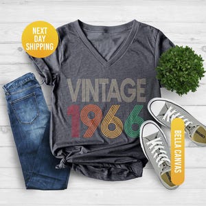 Pu&ograve; includere: T-shirt girocollo grigio scuro melange con la scritta "VINTAGE 1966" in un design retr&ograve;. La maglietta &egrave; abbinata a jeans blu e scarpe da ginnastica in tela grigie. La maglietta &egrave; in materiale Bella Canvas.