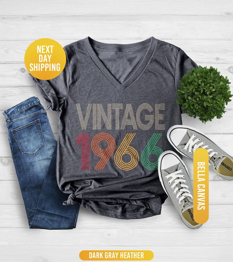 Pu&ograve; includere: T-shirt girocollo grigio scuro melange con la scritta "VINTAGE 1966" in un design retr&ograve;. La maglietta &egrave; abbinata a jeans blu e scarpe da ginnastica in tela grigie. La maglietta &egrave; in materiale Bella Canvas.
