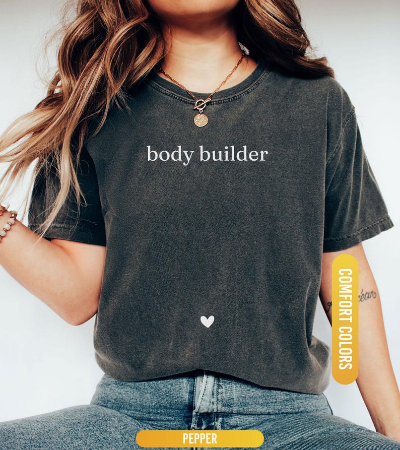 Pu&ograve; includere: T-shirt grigio scuro con la scritta bianca "body builder". Un piccolo cuore bianco &egrave; sotto il testo. La maglietta &egrave; etichettata "Comfort Colors" e "Pepper".