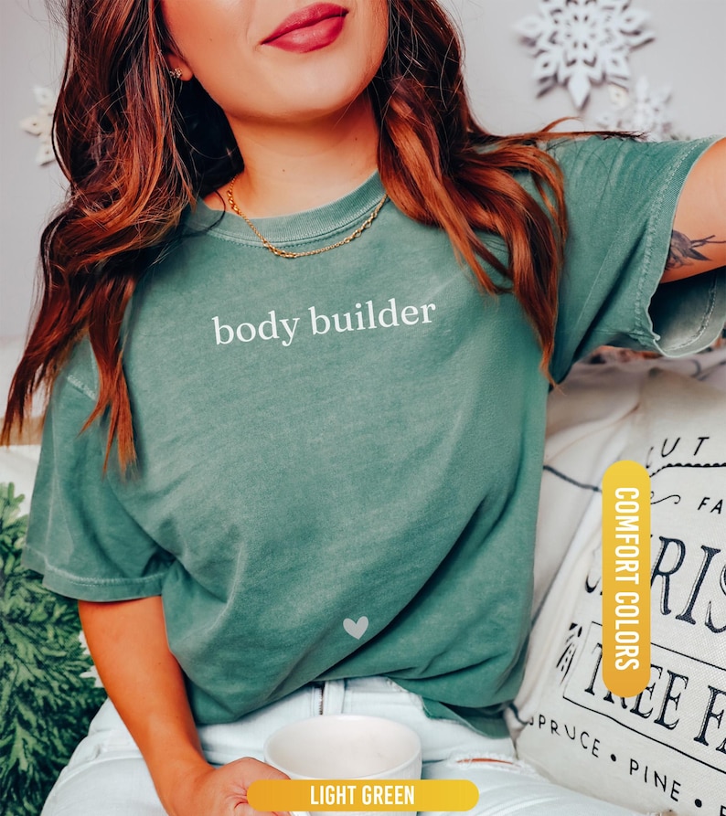 Pu&ograve; includere: T-shirt verde chiaro con la scritta "body builder" in bianco. La maglietta ha un piccolo cuore bianco. La maglietta &egrave; un colore confortevole ed &egrave; verde chiaro.