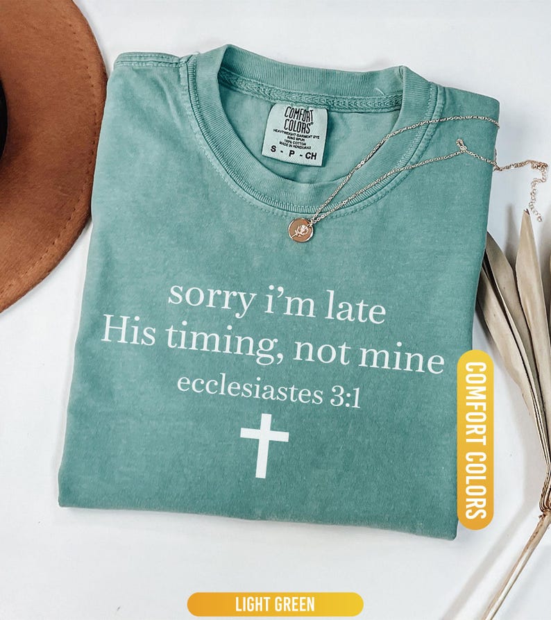 May include: Light green t-shirt with the text "sorry i'm late His timing, not mine ecclesiastes 3:1" and a white cross. A gold necklace with a pendant is on the shirt. The shirt is labeled "Comfort Colors".