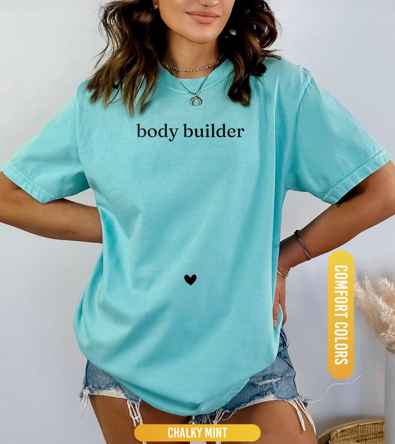 Pu&ograve; includere: Una maglietta azzurra con le parole "body builder" stampate in nero. Un piccolo cuore nero &egrave; sotto il testo. La maglietta &egrave; etichettata "Comfort Colors" e "Chalky Mint".
