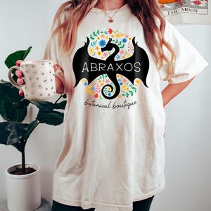 -shirt de la boutique botanique Abraxos | SOUS LICENCE OFFICIELLE | Sarah J. Maas - Les treize wyvernes - Ras du cou - Manon Dragon Kingdom of Ash ToG