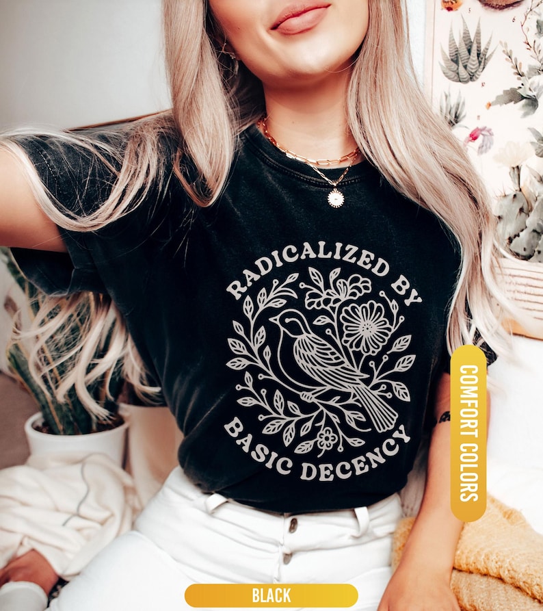 May include: Black t-shirt with a white graphic of a bird, flowers, and the text "RADICALIZED BY BASIC DECENCY". The shirt is labeled "BLACK" and "COMFORT COLORS".