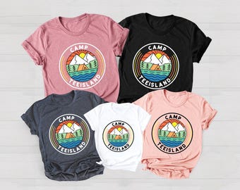 May include: Five t-shirts in various colors: dusty rose, black, navy, white, and peach. Each shirt features a circular graphic with a mountain, sun, lake, and trees design, with the words "CAMP TEEISLAND" in a circle around the design.