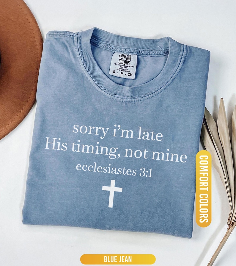 May include: Blue jean Comfort Colors t-shirt with the text "sorry i'm late His timing, not mine ecclesiastes 3:1" and a white cross. The shirt is folded and has a tag that says "Comfort Colors".