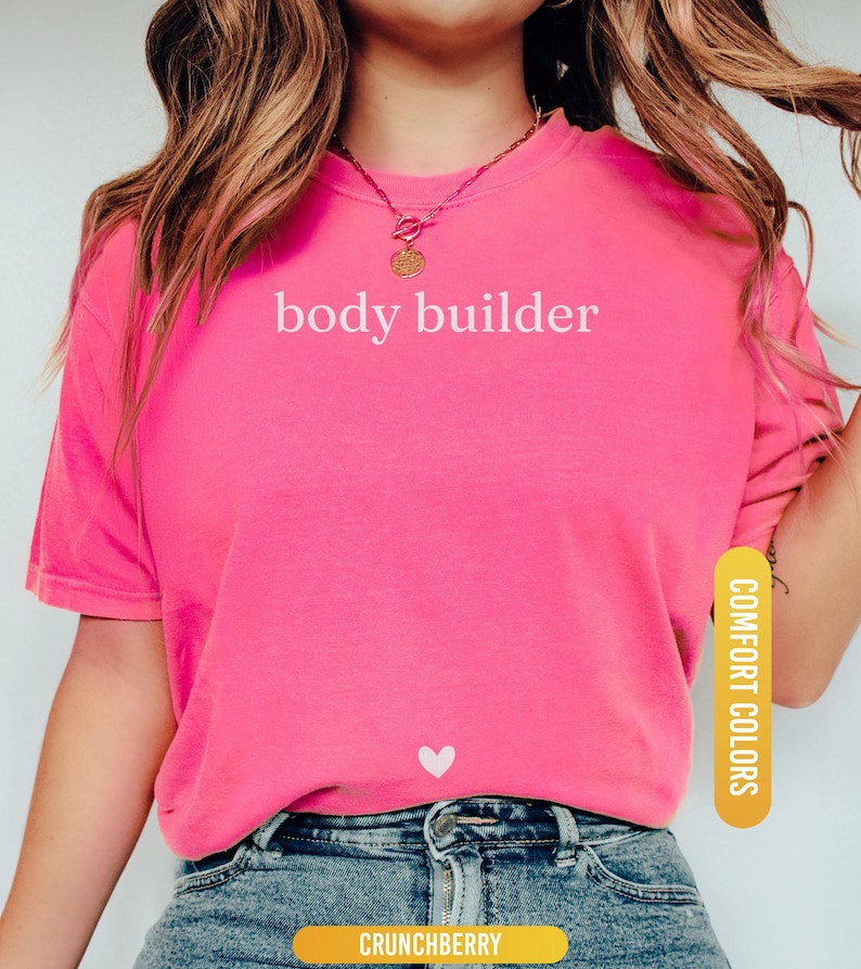 Pu&ograve; includere: Una maglietta rosa acceso con la scritta bianca "body builder". Un piccolo cuore bianco &egrave; sotto il testo. La maglietta &egrave; abbinata a jeans blu. Le parole "Comfort Colors" e "Crunchberry" sono stampate sulla maglietta.