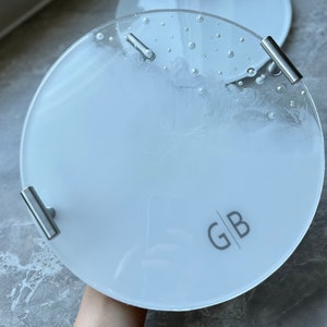 May include: A white round tray with two silver handles and the initials "GB" printed on the surface.