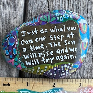 May include: Painted rock with a motivational quote: "Just do what you can one step at a time. The sun will rise and we will try again." The rock is decorated with colorful flowers and swirls. The rock is about 3 inches in diameter.