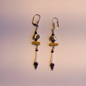 May include: A pair of dangle earrings with a gold seashell charm, a yellow felt accent, and a white bone-like bead with dark blue accents.